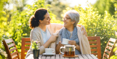 Happy young woman and her mother drinking tea in summer morning